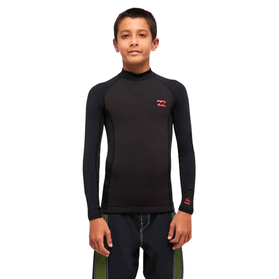A boy modeling a black long-sleeve wetsuit top with a mock neck and a small red Billabong logo on the left chest, paired with dark pants, against a plain white background.