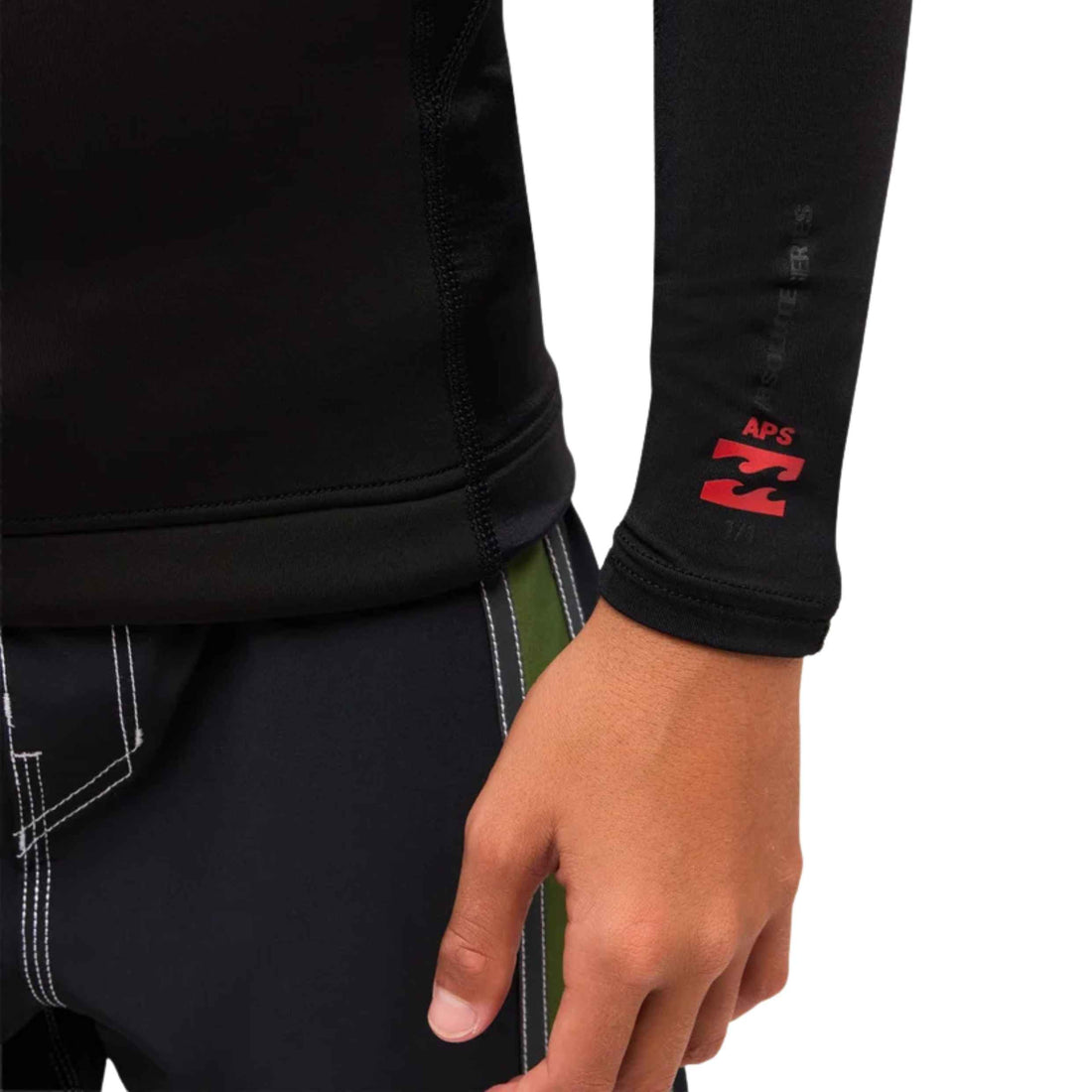 Close-up of a person wearing a black long-sleeve rash top with a red Billabong APS logo on the cuff, paired with dark shorts.