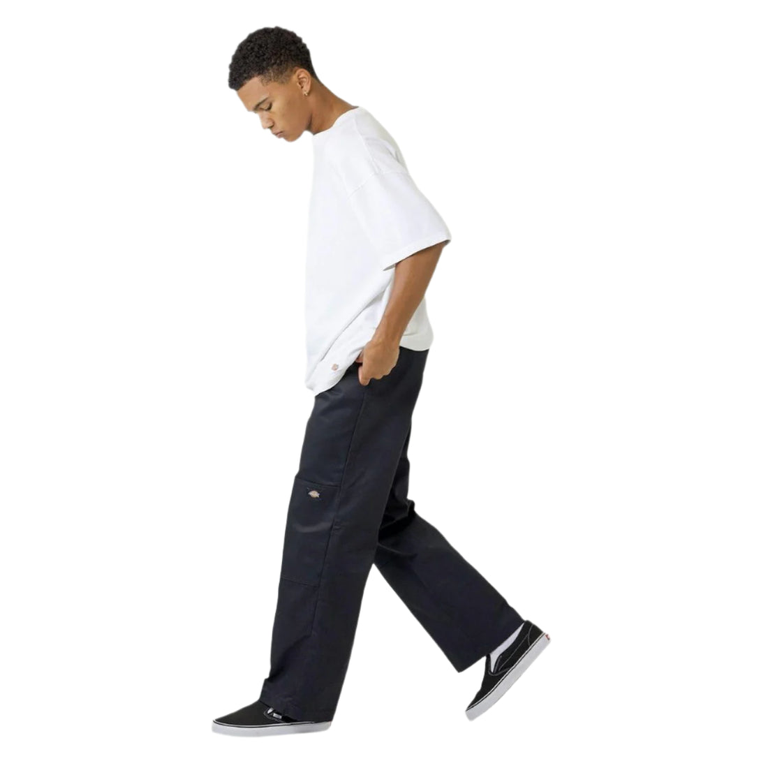 A person walking side-on, wearing a white t-shirt and black Dickies work pants with multiple pockets.