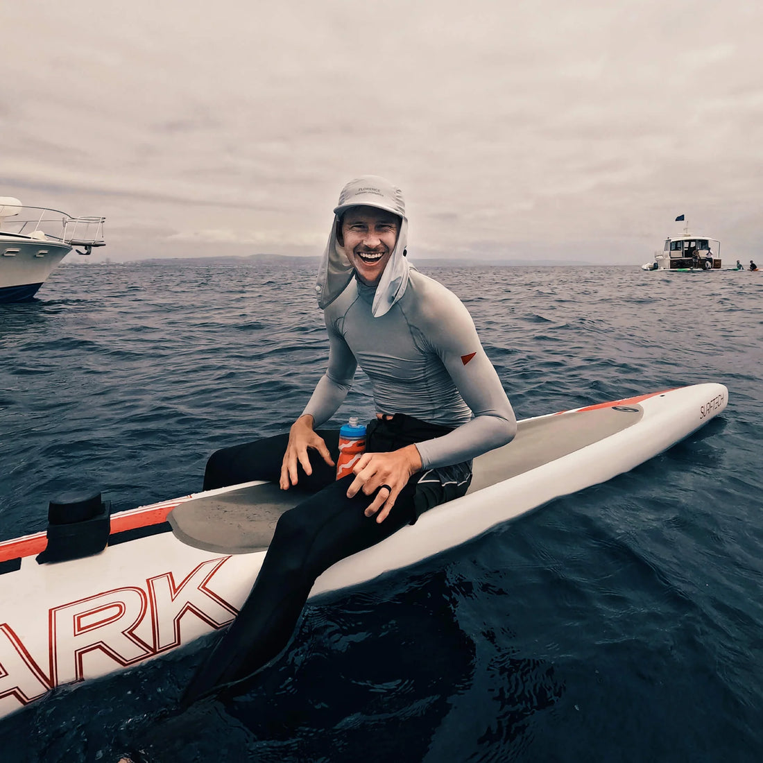 Person sitting on a surfboard in the ocean with a cloudy sky