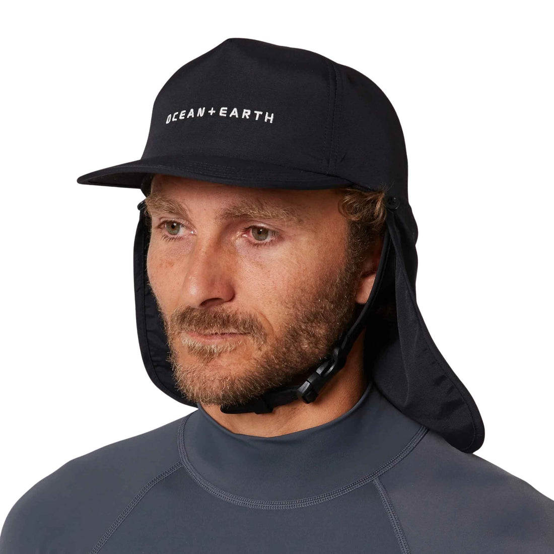 A man wearing a black Ocean Earth sun hat with a neck flap and chin strap, paired with a dark gray wetsuit top, against a solid white background.