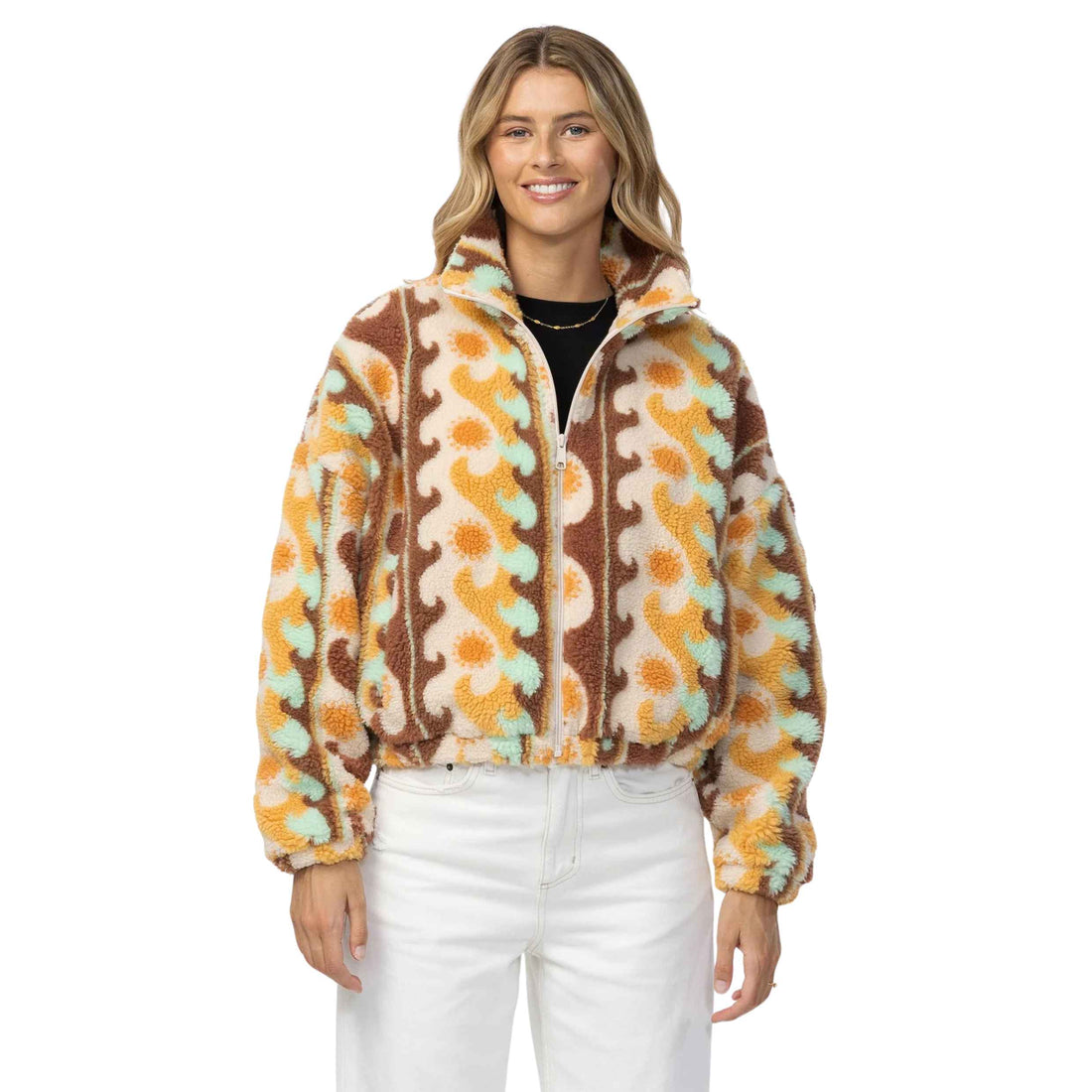 A woman modeling a fuzzy quarter-zip fleece jacket with a retro wavy pattern in brown, orange, and mint green on a cream background, paired with white pants against a solid white studio background.