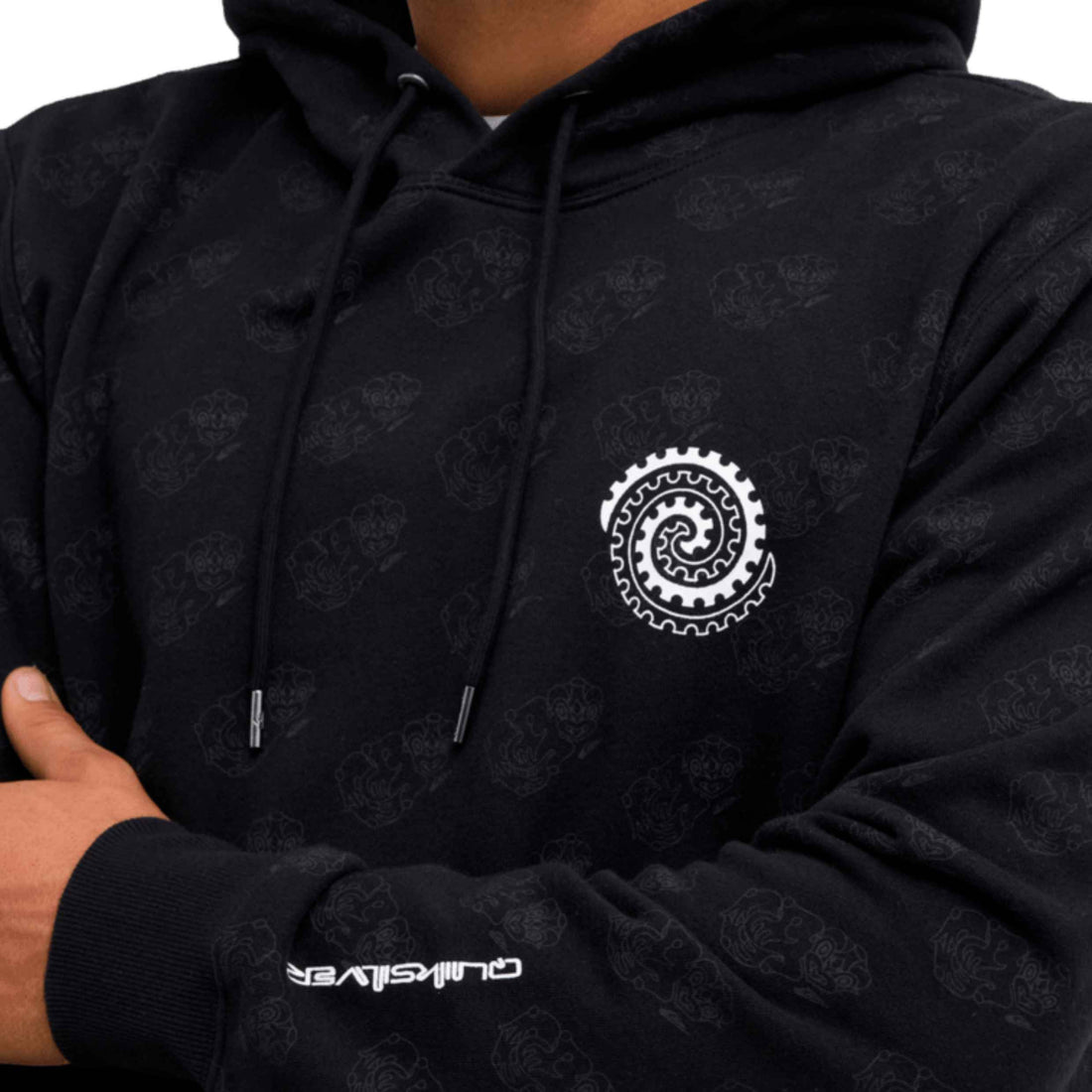 Close-up of a black hoodie worn by a model, featuring a white spiral gear graphic on the left chest and a white 'QUIKSILVER' logo on the right sleeve cuff.