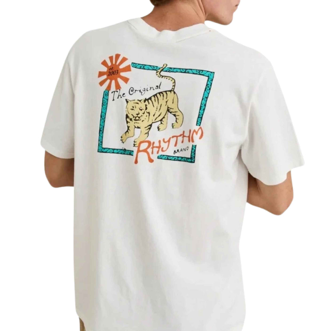 A person wearing an oversized white graphic T-shirt, shown from the back. The shirt features a large retro-style print with a tiger, a turquoise border, orange text reading 'The Original RHYTHM MAN,' and an orange sunburst.