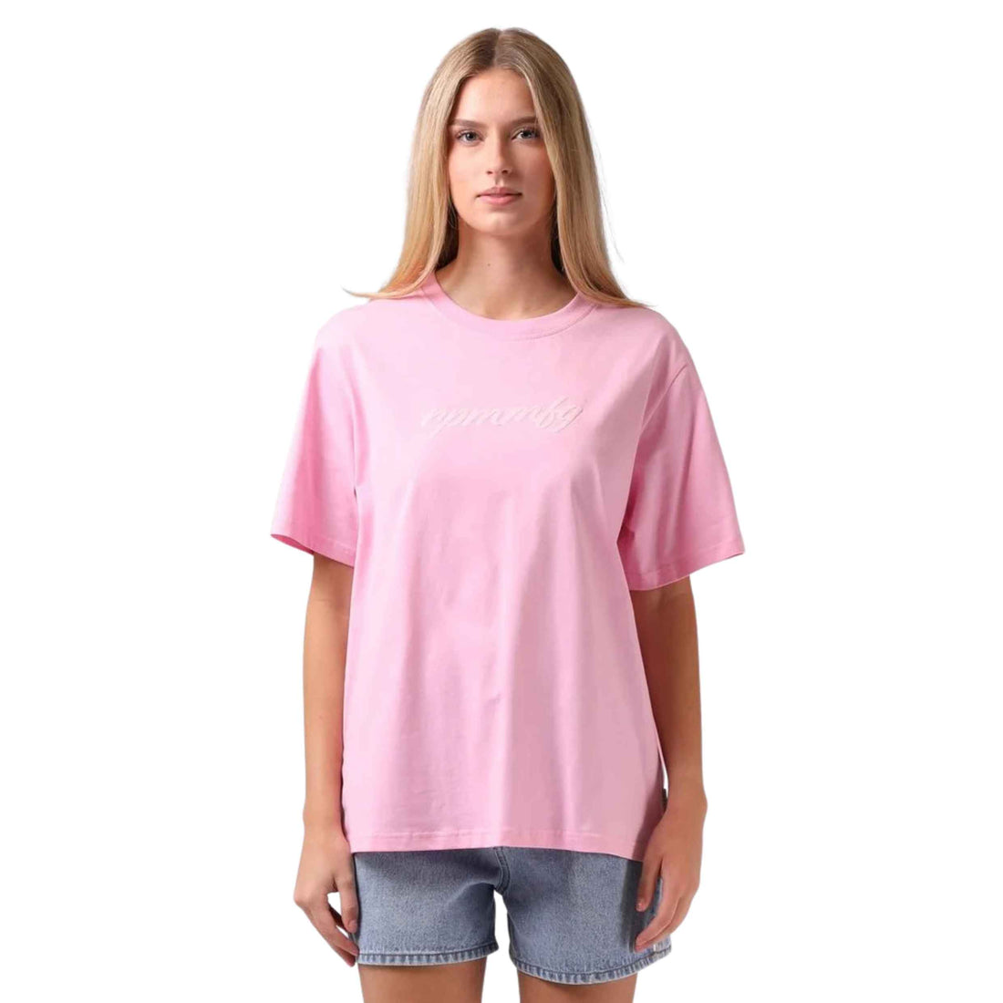 A woman modeling a light pink short-sleeve t-shirt with 'innately' written in white script across the chest, paired with denim shorts against a solid white background.