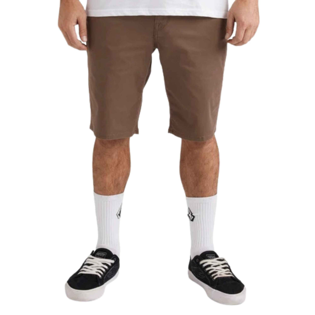 A person from waist to feet wearing brown knee-length shorts, white crew socks, and black low-top sneakers against a plain white studio background.